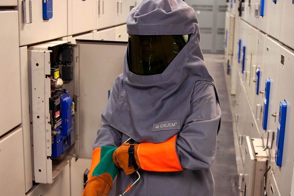 An electrical worker wearing Arc Flash PPE suit, visor and gloves